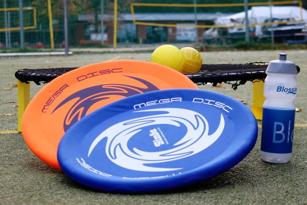 Zwei Frisbeescheiben und zwei Spikeballs liegen auf einem Sportplatz.
