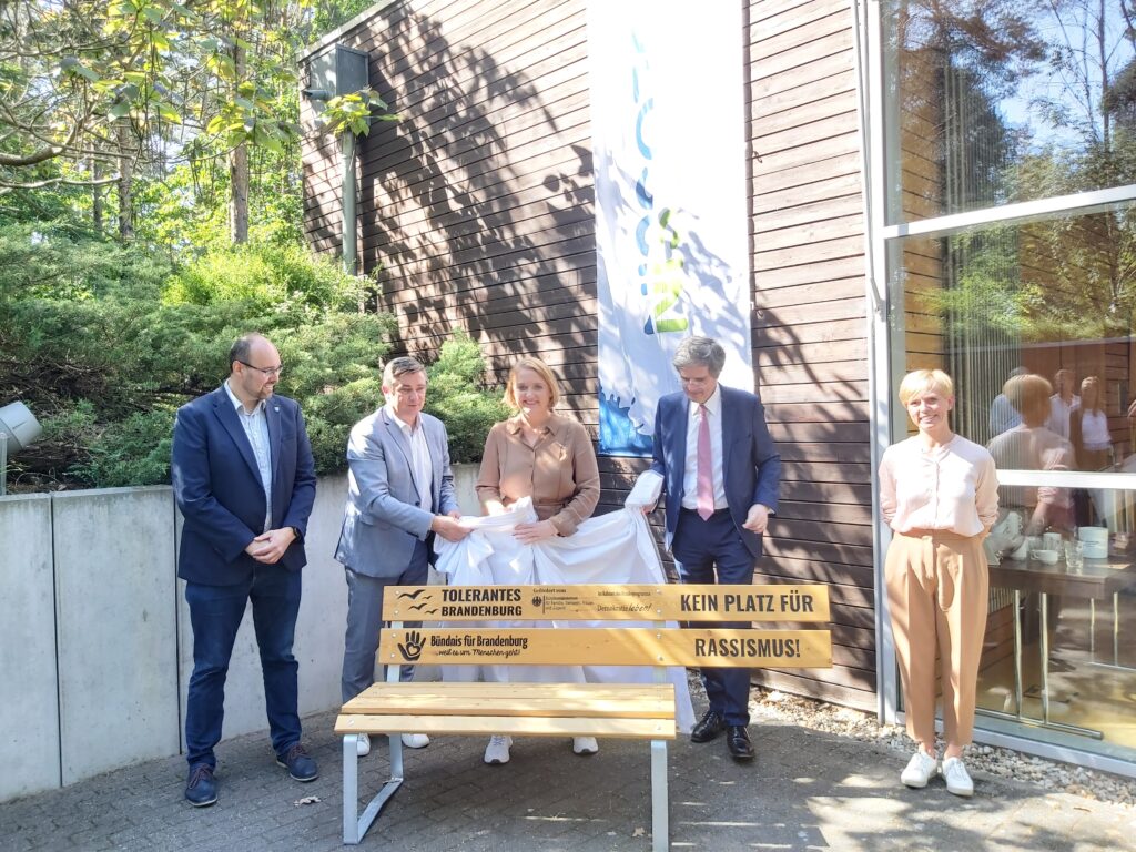 Fünf Personen präsentieren eine Bank mit Aufschrift "Kein Platz für Rassismus".