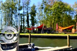 Glas mit der Beschriftung "Blossiner Molle" am Wasser mit Blick auf das Hafencafe namens Palstek.