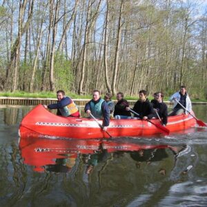 Eine Gruppe paddelt gemeinsam in einem roten Kanadier auf dem See.
