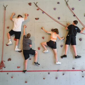 Jugendliche klettern gemeinsam an einer Indoor-Kletterwand.