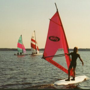 Person windsurft auf dem See, im Hintergrund sind weitere Segelboote.