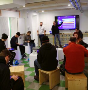 Eine Gruppe sitzt und arbeitet mit Tablets, während vorne eine Präsentation läuft.