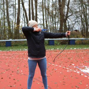 Person spannt einen Bogen beim Bogenschießen auf dem Sportplatz.