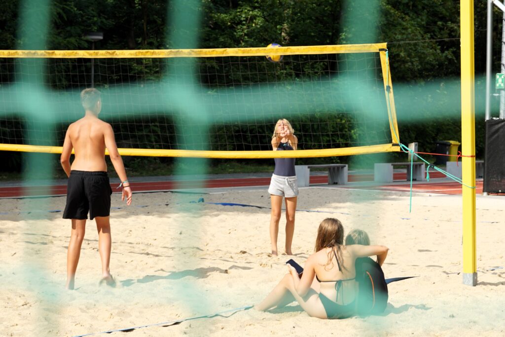 Jugendliche spielen Volleyball auf einem Beachvolleyballfeld.