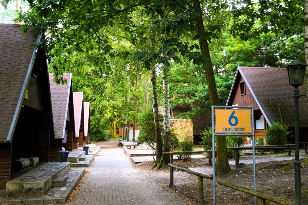 Weg zum Jugenddorf mit den einzelnen Holzhäusern und Bäumen.