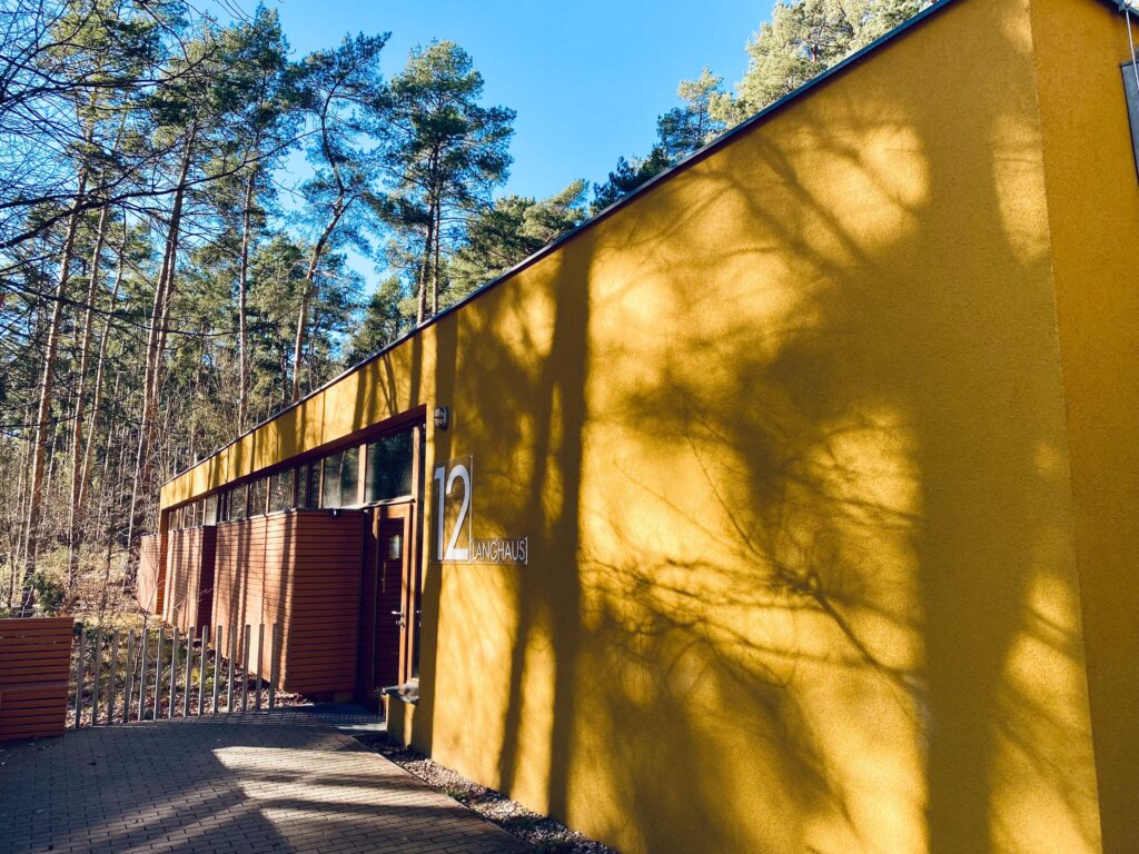 Ein längliches Gebäude als Schlafmöglichkeit umgeben von Bäumen namens Langhaus.