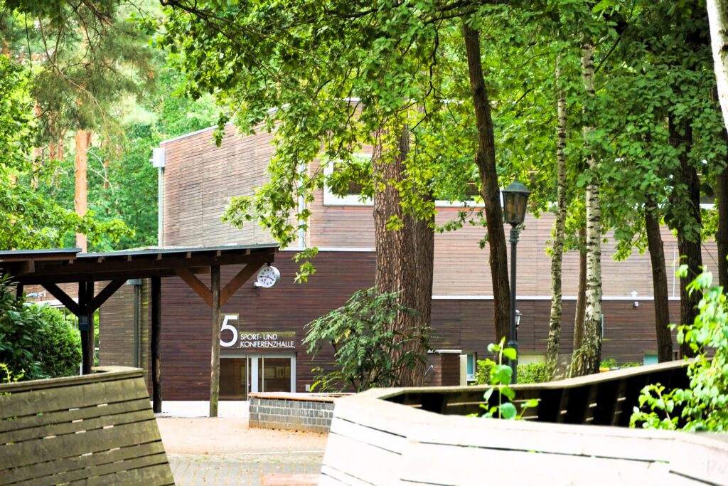 Sport- und Konferenzhalle von außen, umgeben von Bäumen.