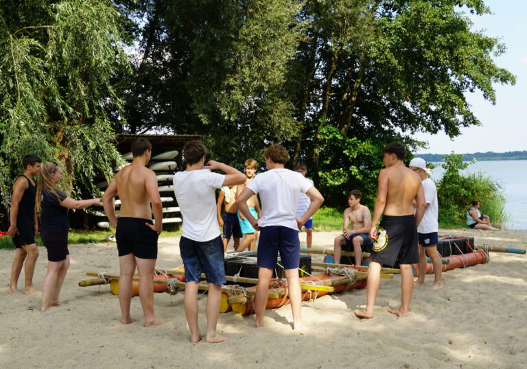 Eine Gruppe Jugendlicher steht um zwei Flöße herum.